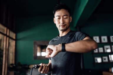 A man in athletic wear checks his smartwatch while holding a jump rope in a gym setting.