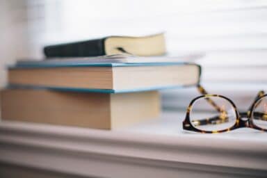 Tortoiseshell glasses sit on a windowsill next to a stack of books, representing cognitive health and memory.