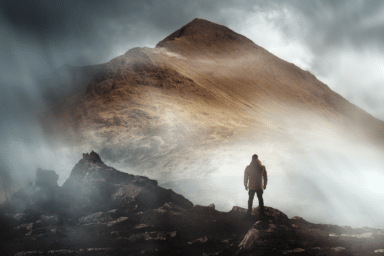 A person stands on a rocky peak looking toward a massive, light-filled mountain shrouded in mist.
